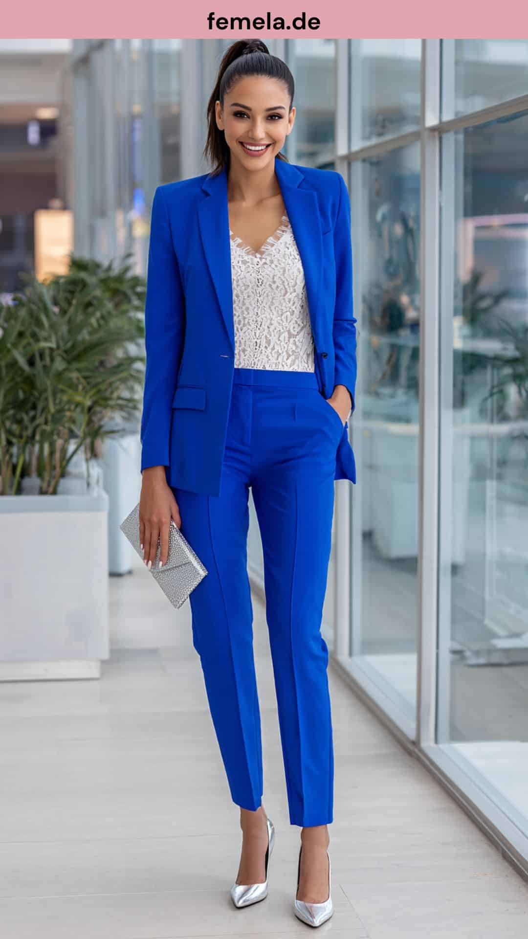 Frau im königsblauen Hosenanzug mit silbernen High Heels in einer modernen Büro-Umgebung.