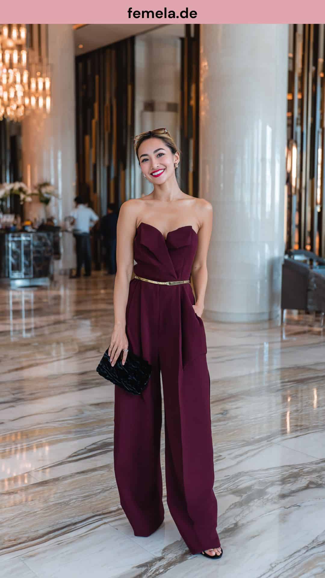 Ein burgunderroter Jumpsuit mit weitem Bein und Goldgürtel als stilvolle Alternative zum Abendkleid.