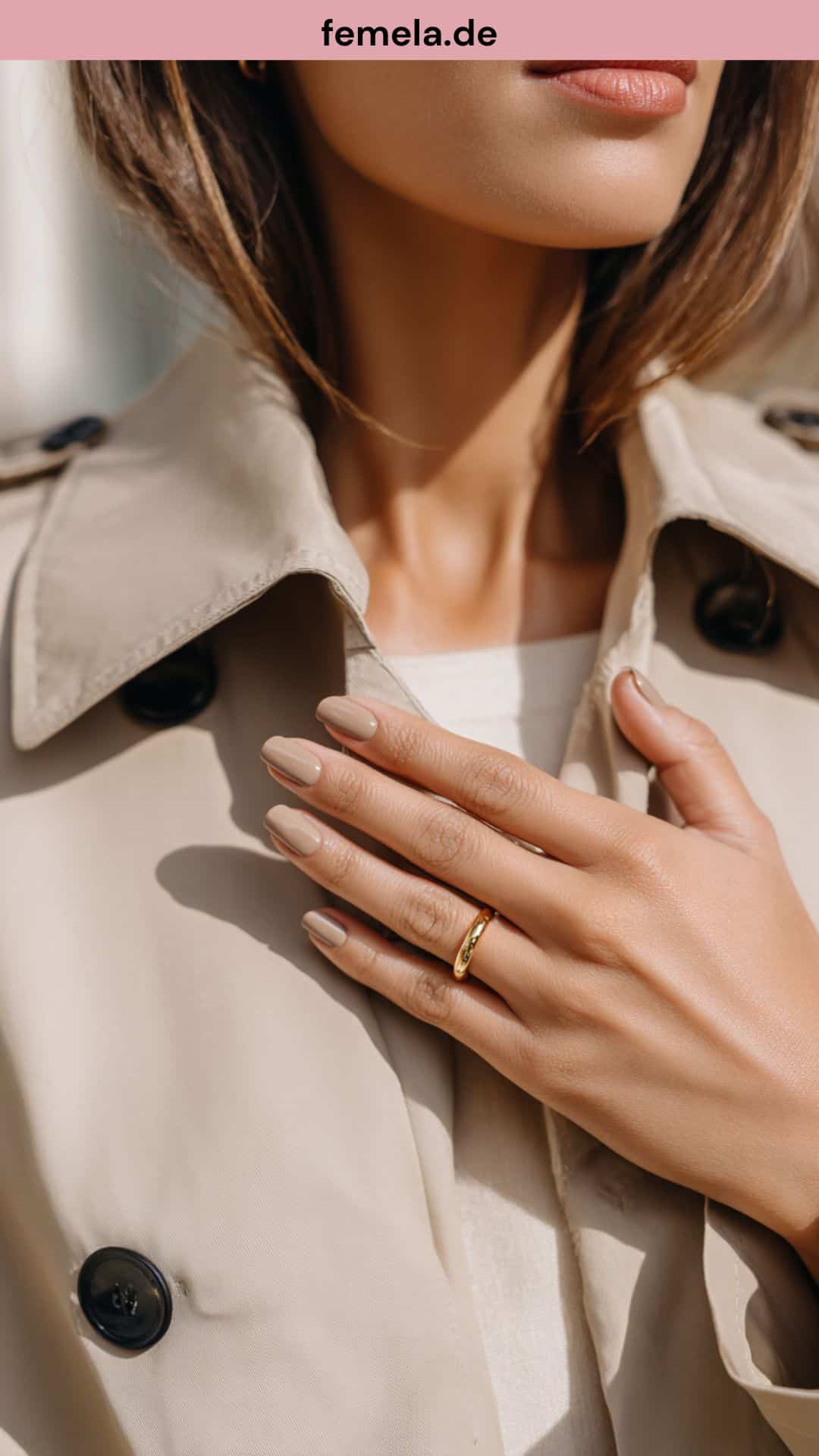 Elegante Hand mit Nude-Nägeln, die einen Trenchcoat berührt.