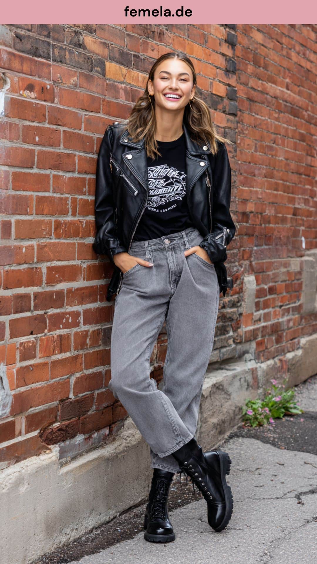 Cooler Streetstyle-Look mit grauer Used-Look Jeans, Band-Shirt und schwarzer Lederjacke vor einer Backsteinwand.